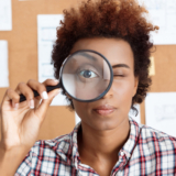 Young beautiful african worker holding magnifier infront of eye.