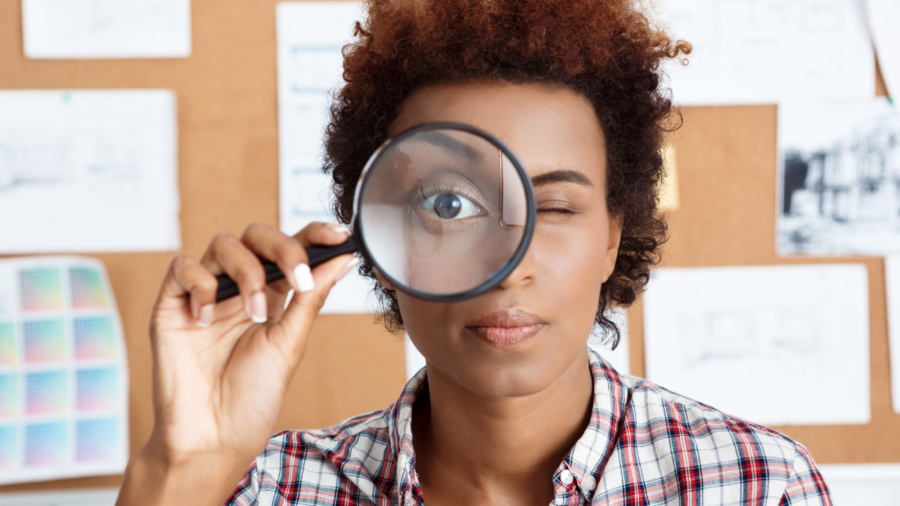 Young beautiful african worker holding magnifier infront of eye.